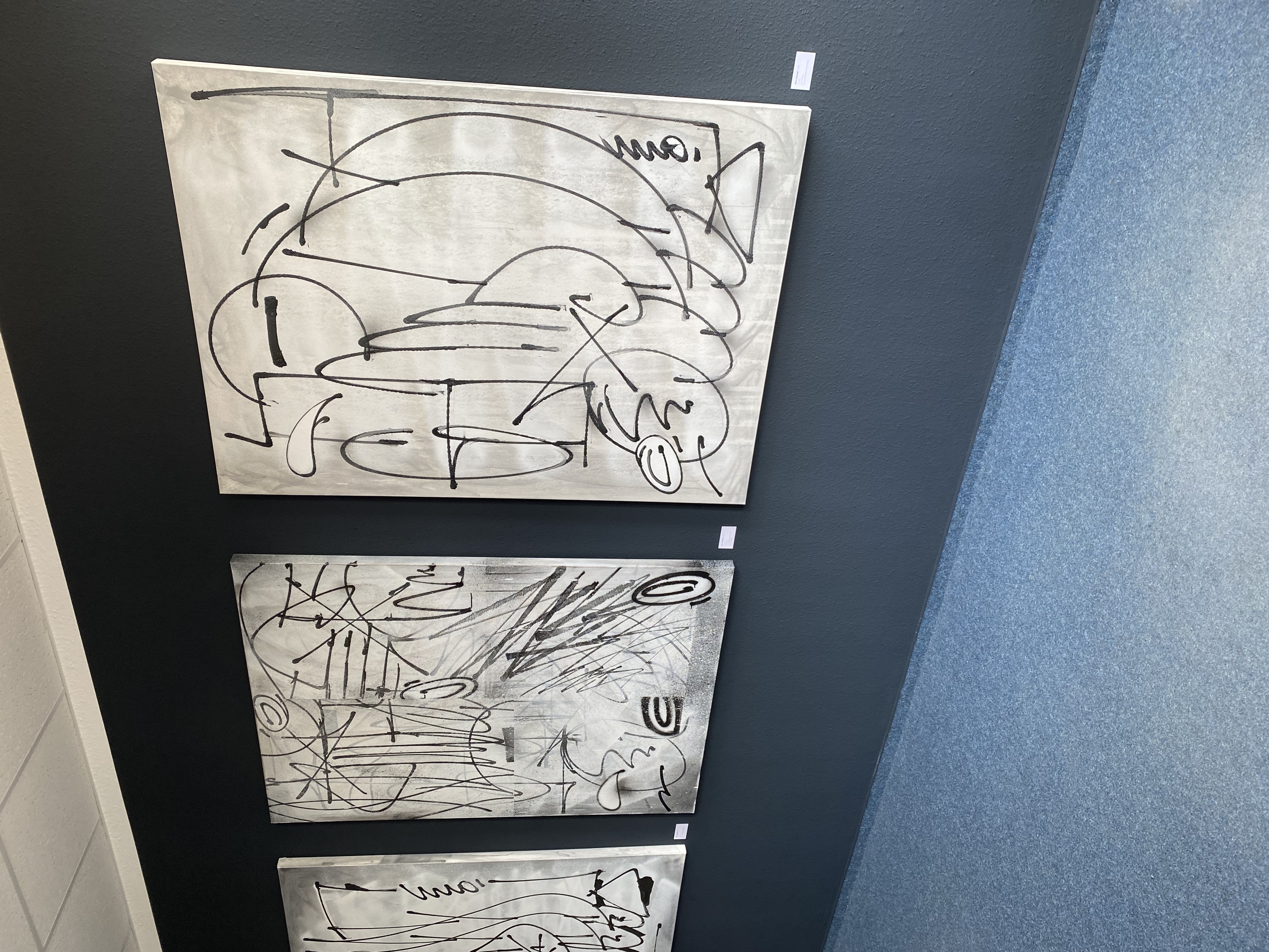 Drei schwarz weiße Kunstwerke hängen an einer dunklen Wand.